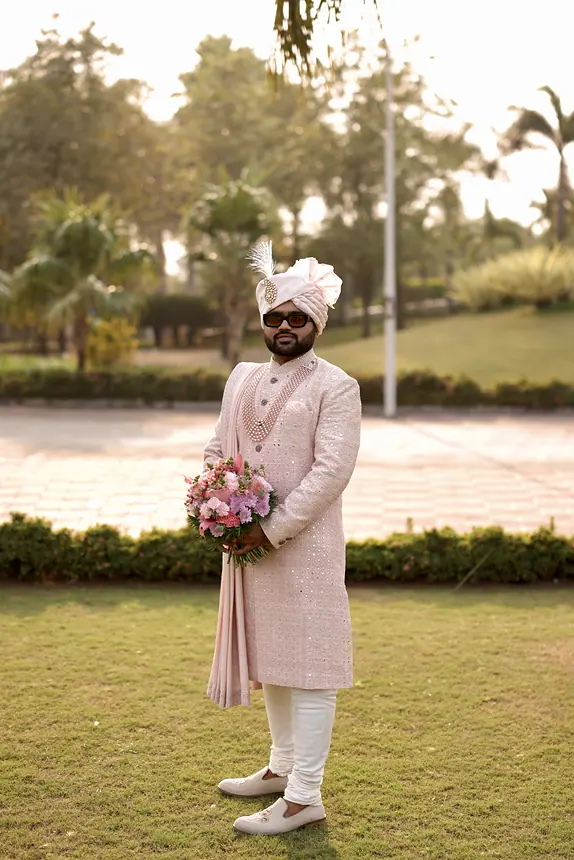 Groom in blush sherwani with a bouquet in the garden